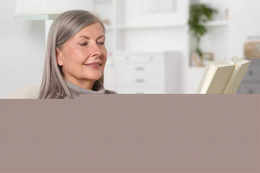 Beautiful senior woman reading book in armchair at home