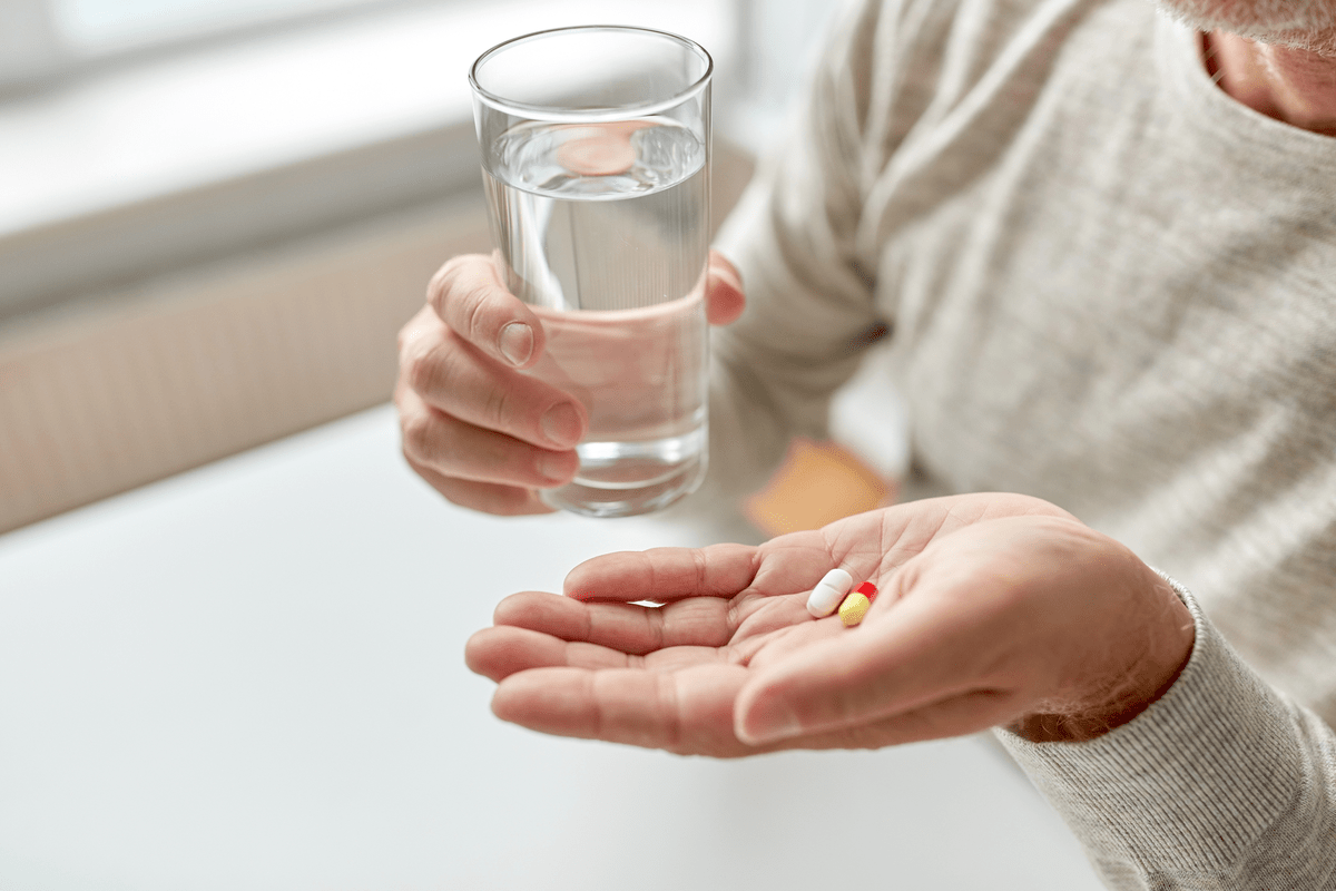 Close up of old man hands with pills and water